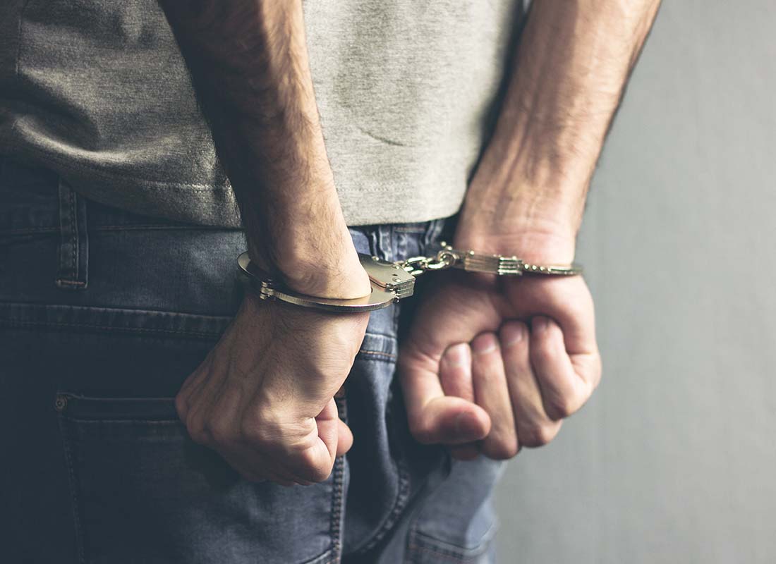 Crime Insurance - Close-up of Young Man in T-Shirt and Jeans with Hands in Handcuffs Placed behind His Back