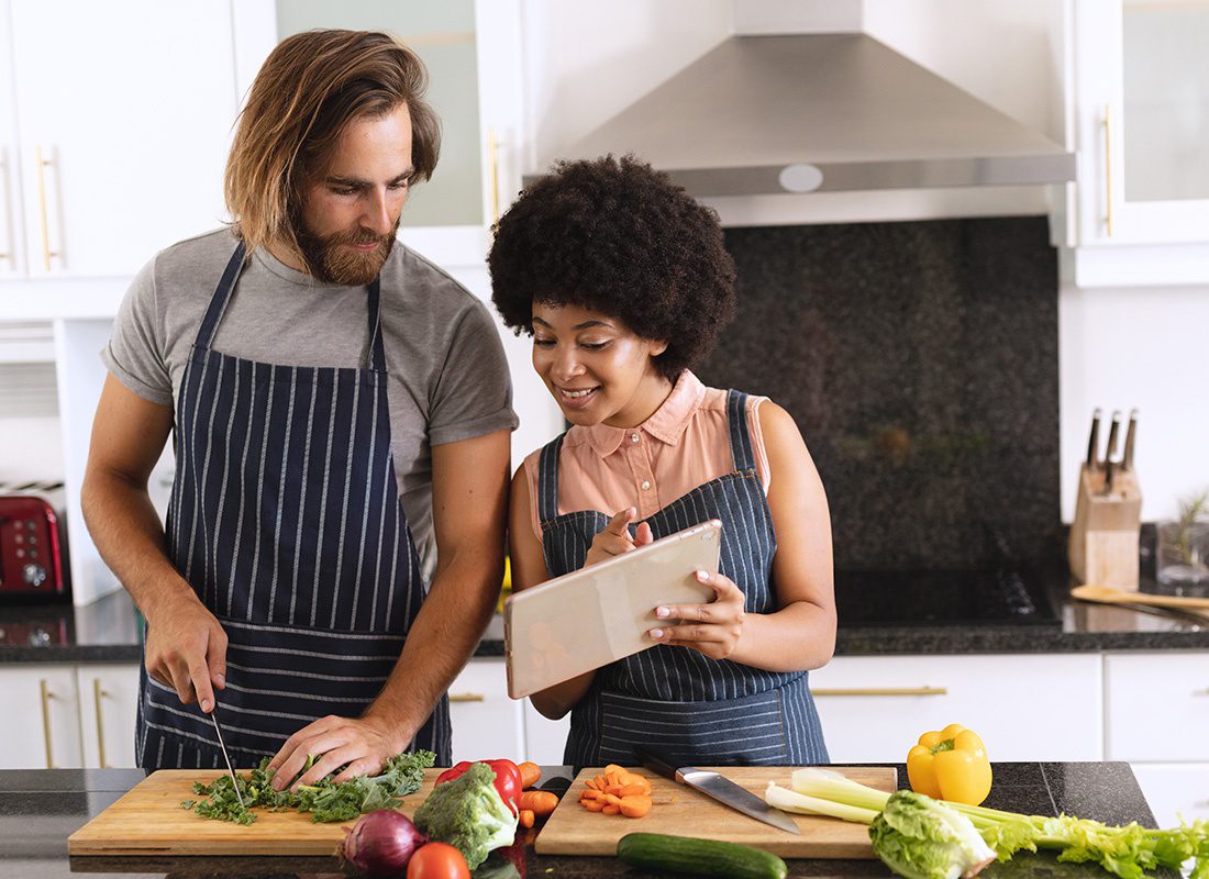 About Our Agency - Happy Couple Prepare a Meal in the Kitchen as They Look at a Tablet for the Recipe