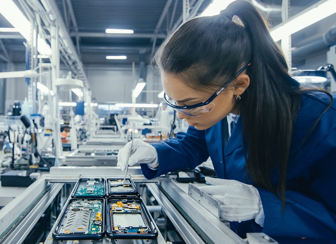 Insurance by Industry - Electronics Factory Workers Assembling Circuit Boards by Hand While it Stands on the Assembly Line